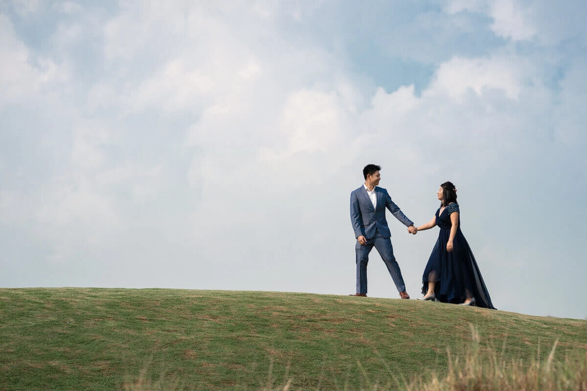 A formally dressed couple holding hands on a grassy hilltop.